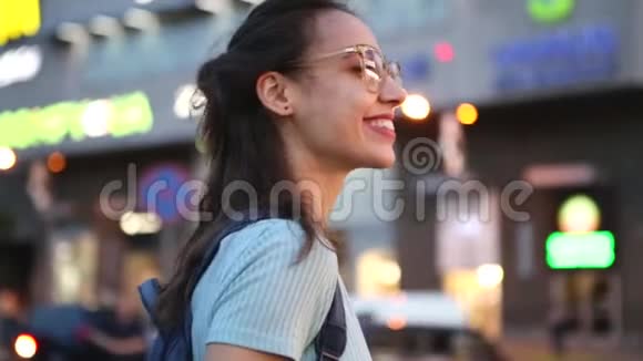 户外城市肖像一位戴眼镜的年轻成年美女在夜间城市灯光下在街上摆姿势视频的预览图