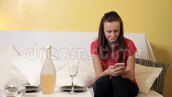 一个年轻的女孩摆好桌子吃晚饭拿着电话坐在沙发上家庭晚餐浪漫晚餐视频的预览图