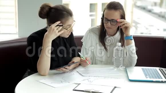两个戴眼镜的女商人坐在一起讨论生意使用平板电脑和笔记本电脑绘制商业发展图表视频的预览图