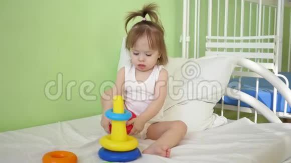 小宝宝坐在医院病房的床上玩金字塔生病的女孩在医院里康复视频的预览图