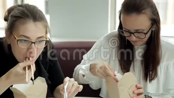 两个戴着眼镜的年轻商务女孩坐在笔记本电脑的咖啡馆里吃着中国面条看着笔记本电脑视频的预览图