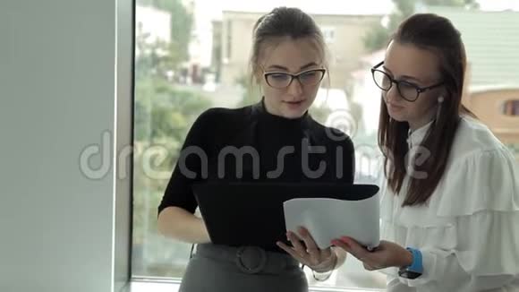 两个戴着眼镜的年轻女商人站在窗口讨论商业发展视频的预览图