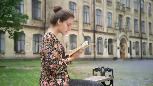 年轻漂亮的女大学生在大学附近的街道上读书看书坐在长凳上视频的预览图