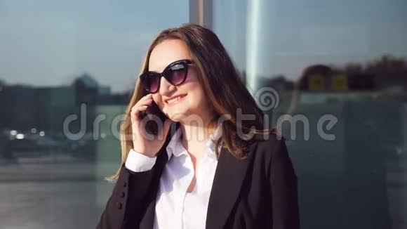 年轻微笑的女商人在电话中交谈的肖像现代智能手机附近的快乐美女说话视频的预览图
