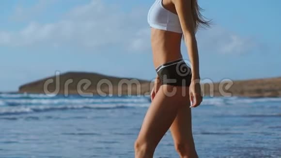 一个女人赤脚在海滩上行走进入海洋的特写镜头流动路线视频的预览图
