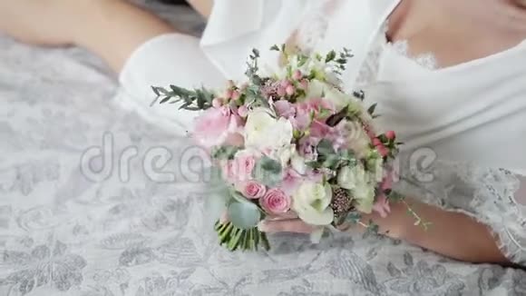 在闺房里一位迷人而性感的新娘躺在床上抚摸着一束美丽的粉红色和白色玫瑰的婚礼花束视频的预览图