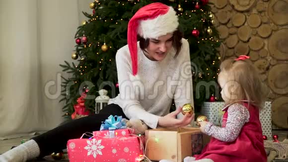 美丽年轻的母亲和孩子带着圣诞树金色玩具和礼物在家里庆祝寒假视频的预览图