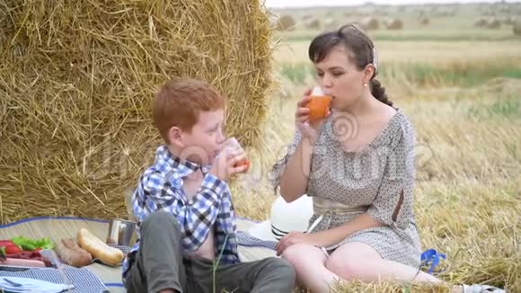 美丽的年轻女子带着红头发的儿子在干草堆中间的野餐中倒灌胡萝卜汁视频的预览图