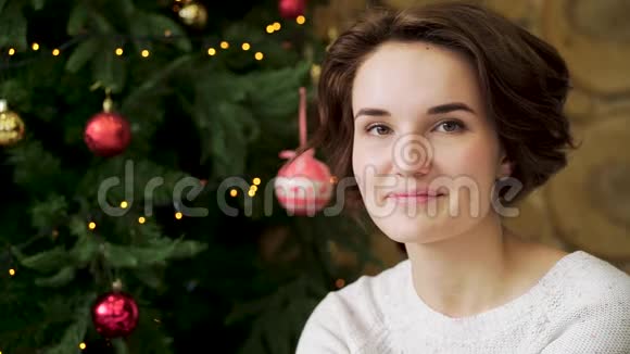 一个美丽的微笑的黑发的女孩在圣诞树前庆祝新年的肖像年轻漂亮的女人视频的预览图