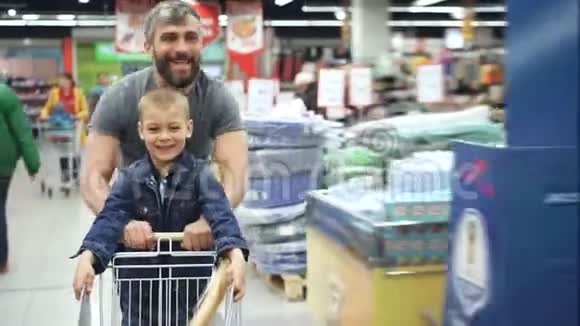 可爱的父亲和他可爱的小儿子在超市里玩得很开心他带着小购物车跑着视频的预览图
