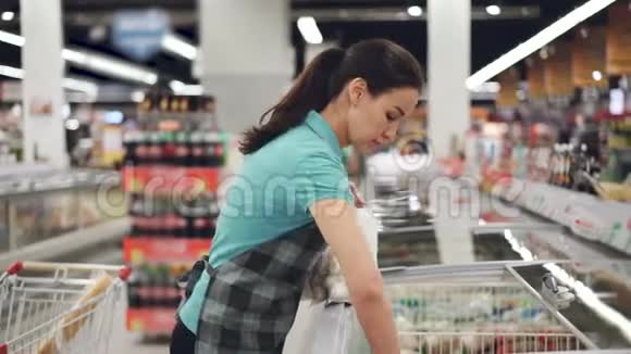穿着围裙的漂亮女售货员正忙着把袋子和预先煮熟的食物放进冰箱货架上的鲜艳产品视频的预览图