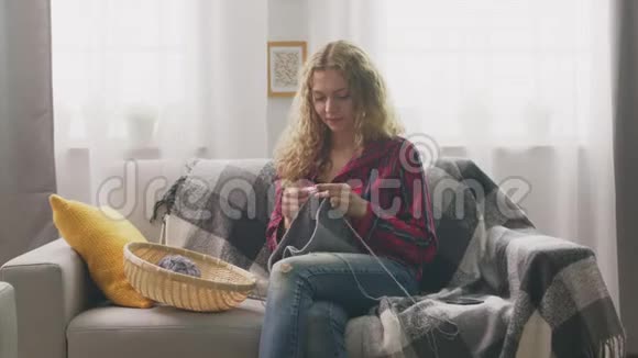 在家里坐在沙发上编织的年轻女子放大视频的预览图