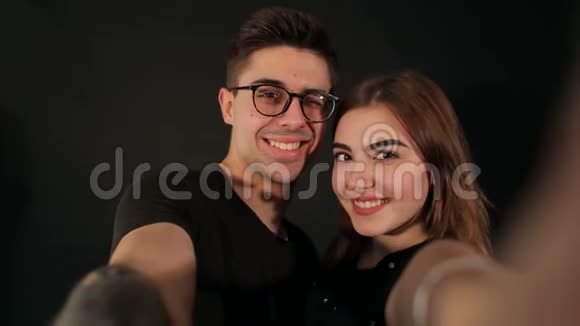 两个快乐情人在黑色背景下在智能手机上自拍的肖像视频的预览图