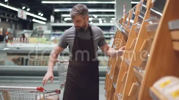 大型超市的男员工正在从购物车里取出新鲜面包并将其放在面包店的货架上视频的预览图