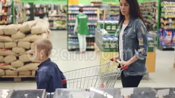 年轻的女士和她穿着牛仔夹克的儿子正在一起购物他们正在超市的过道里走着漂亮视频的预览图