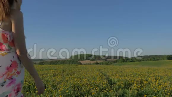 女人穿着礼服走在盛开的黄色田野上转身就位视频的预览图