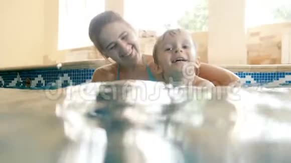 年轻母亲教她的孩子游泳把他抱在水面上的4K镜头视频的预览图
