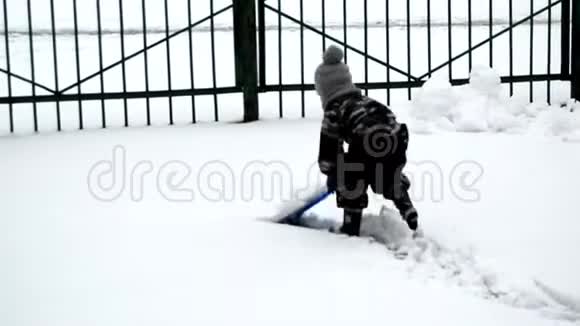 快乐的小男孩穿着冬季连衣裙玩着塑料铲子在冬季公园的雪道上擦雪视频的预览图