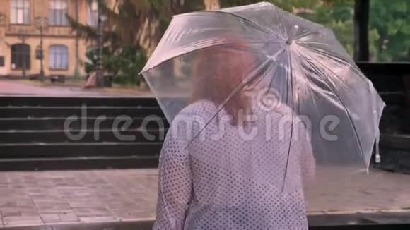 戴着眼镜的肥姜姑娘在雨天的公园里爬上小楼梯撑着伞视频的预览图