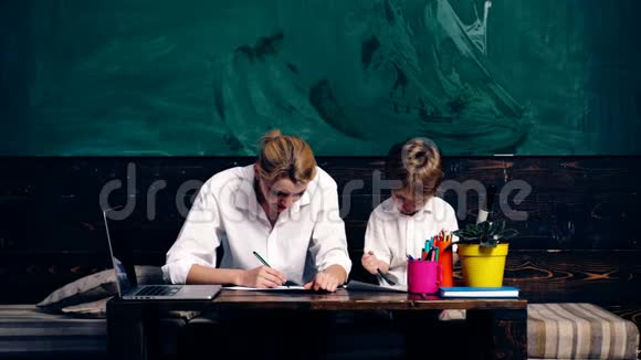 教师与男孩坐在学校课桌上的绿色学校板的背景学习概念视频的预览图