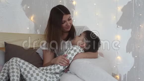 一位美丽的母亲和坐在床上的儿子玩吻他有一个好心情总体计划视频的预览图
