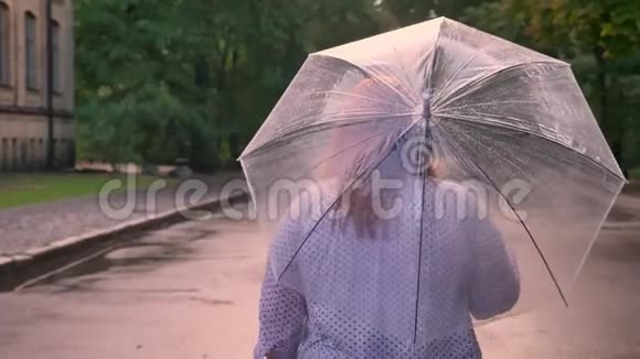 胖姜女的剪影在雨中漫步在公园的路上撑着伞后景视频的预览图