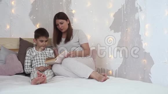 一个穿睡衣的漂亮女孩在坐在床上睡觉前给一个小男孩读一本书总体计划高清高清视频的预览图