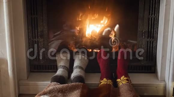 两个人在燃烧的壁炉里穿着羊毛针织袜子暖脚的4K镜头视频的预览图