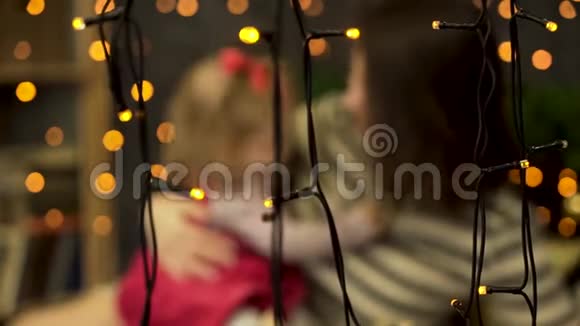 装饰着绿色云杉树枝的房间里黄色花环后面的幸福妈妈和可爱宝宝的模糊画像视频的预览图