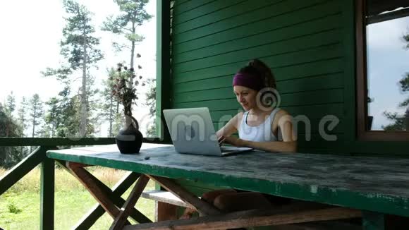 夏日一位微笑的商务女性旅游自由职业者在户外的笔记本电脑上靠在绿色的墙壁上消遣视频的预览图