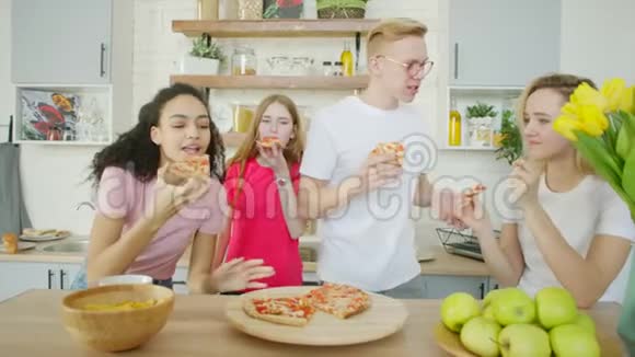 快乐的朋友在吃披萨在厨房里笑视频的预览图