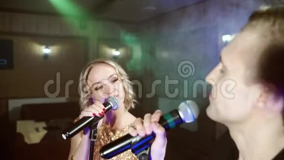 一对年轻夫妇在卡拉OK酒吧里用麦克风唱歌的肖像视频的预览图