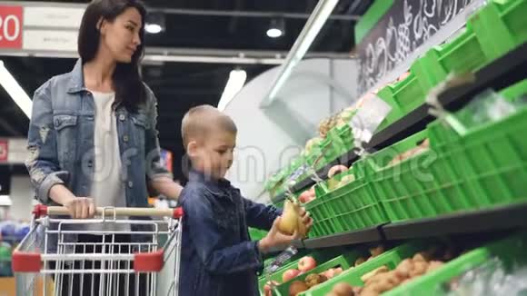 年轻的一家母子正在杂货店买水果他们正在吃梨和猕猴桃然后把它们放进去视频的预览图