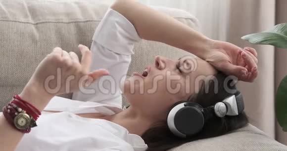女人躺在沙发上用耳机唱歌听歌视频的预览图