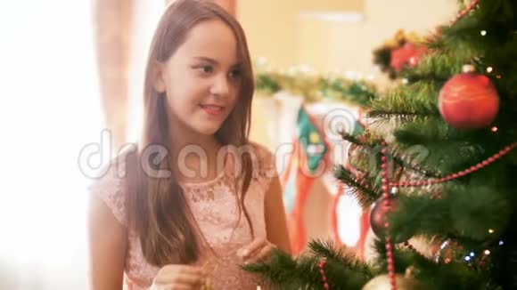 4k视频美丽的黑发少女在客厅的圣诞树上挂着五颜六色的视频的预览图