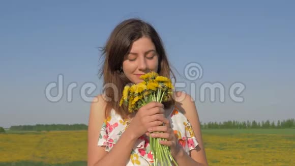 田野里的女人的肖像带着一束黄色的蒲公英花嗅着他视频的预览图