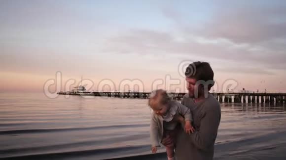 年轻的父亲和小女儿在沙滩上玩耍拥抱和欢笑呕吐视频的预览图
