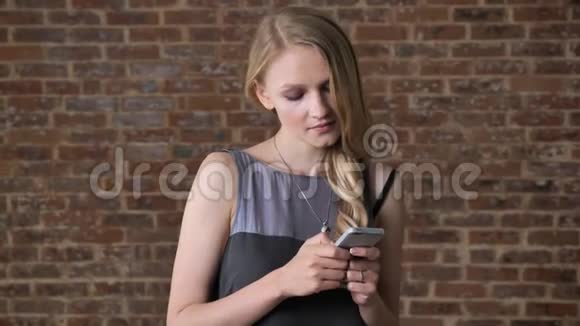 年轻可爱的金发女孩正在智能手机上输入信息思维观念沟通观念砖背景视频的预览图