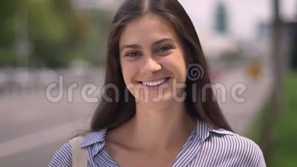 美丽的年轻幸福的女人微笑着看着相机抚摸着头发站在路边的街道上视频的预览图