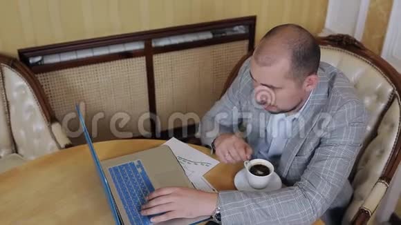 穿西装的年轻人坐在办公室拿着笔记本电脑喝着咖啡视频的预览图