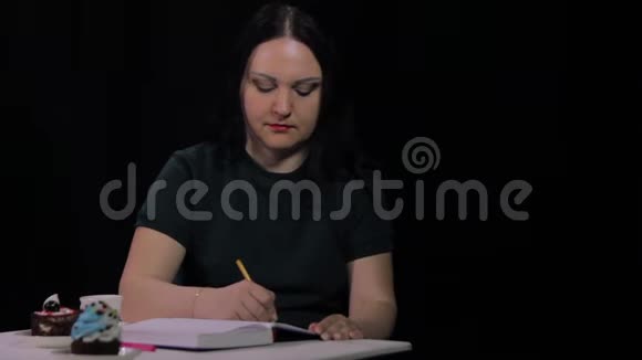 咖啡馆里的一个女人在黑色背景下喝着白色杯子里的咖啡然后写日记视频的预览图
