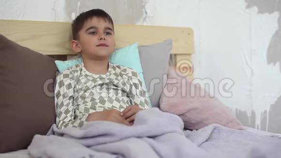 一个生病的小男孩坐在床上咳嗽用毯子盖住自己高清高清视频的预览图