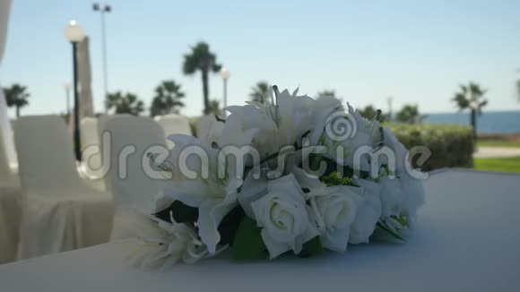 婚礼上的白色百合花和白色玫瑰花束装饰桌布在模糊阳光的度假村背景上视频的预览图