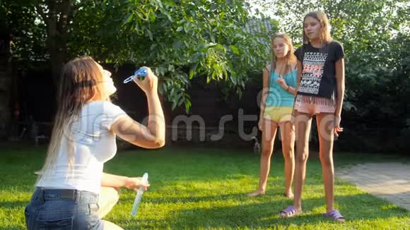 两个十几岁的女孩在操场草地上肥皂泡后奔跑和跳跃的慢动作镜头视频的预览图