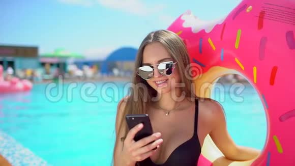 美丽的年轻女子在夏季Wih智能手机比基尼女孩在泳池边用电话女人在手机上发短信视频的预览图