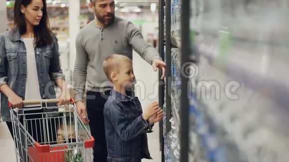 可爱的孩子正从超市的货架上拿一瓶水放进购物车他可爱的父母视频的预览图