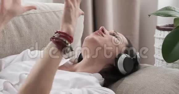 女人躺在沙发上一边唱歌一边听着耳机里的音乐视频的预览图