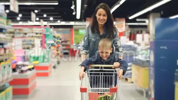 可爱的妈妈和她可爱的小儿子在超市里玩得很开心她带着小购物车跑着视频的预览图