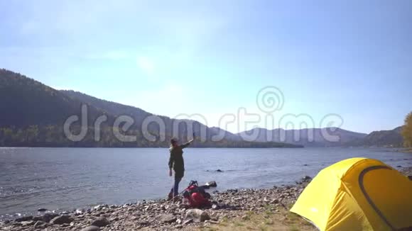 带着红色背包的女旅行者去了山湖的海岸然后它在智能手机上拍摄视频视频的预览图