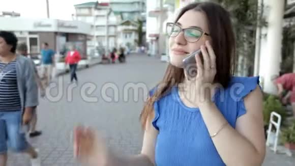 一个年轻的女孩走在海边的一个城市通过电话交谈分享她的印象视频的预览图